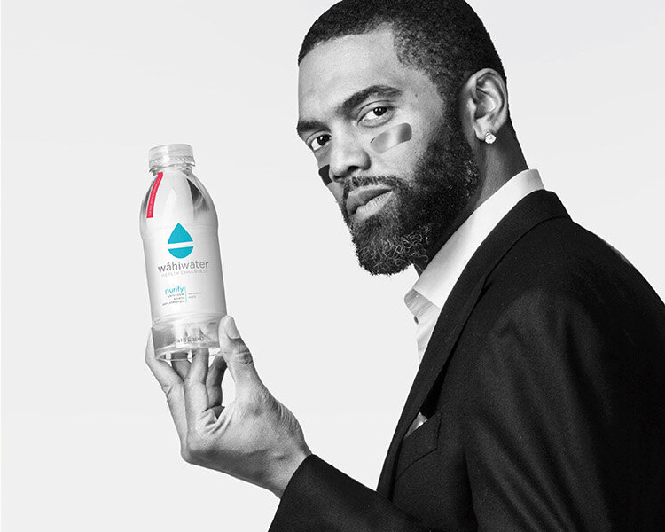 Randi Moss WahiWater Branding Session – Charlotte Commercial Photography Black and white commercial branding photo of Randi Moss holding a WahiWater bottle against a dark studio backdrop.