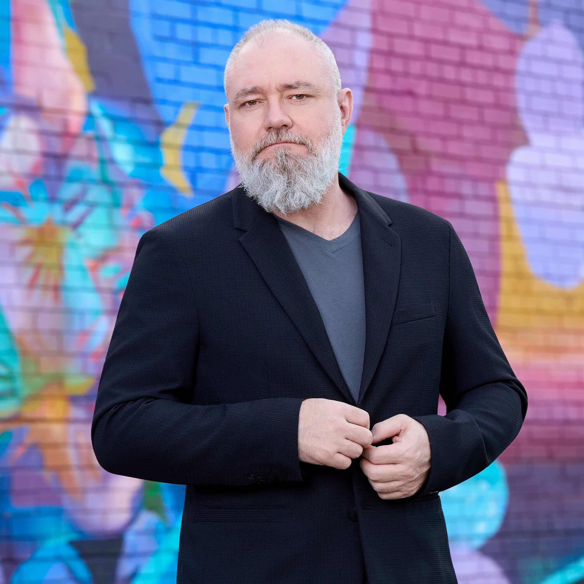 Ryan Sumner Creative Director Portrait – Charlotte Corporate Photography Outdoor environmental portrait of Ryan Sumner, Creative Director of Fenix Fotography, posing in a dark suit jacket against a colorful painted brick mural in Charlotte, NC.