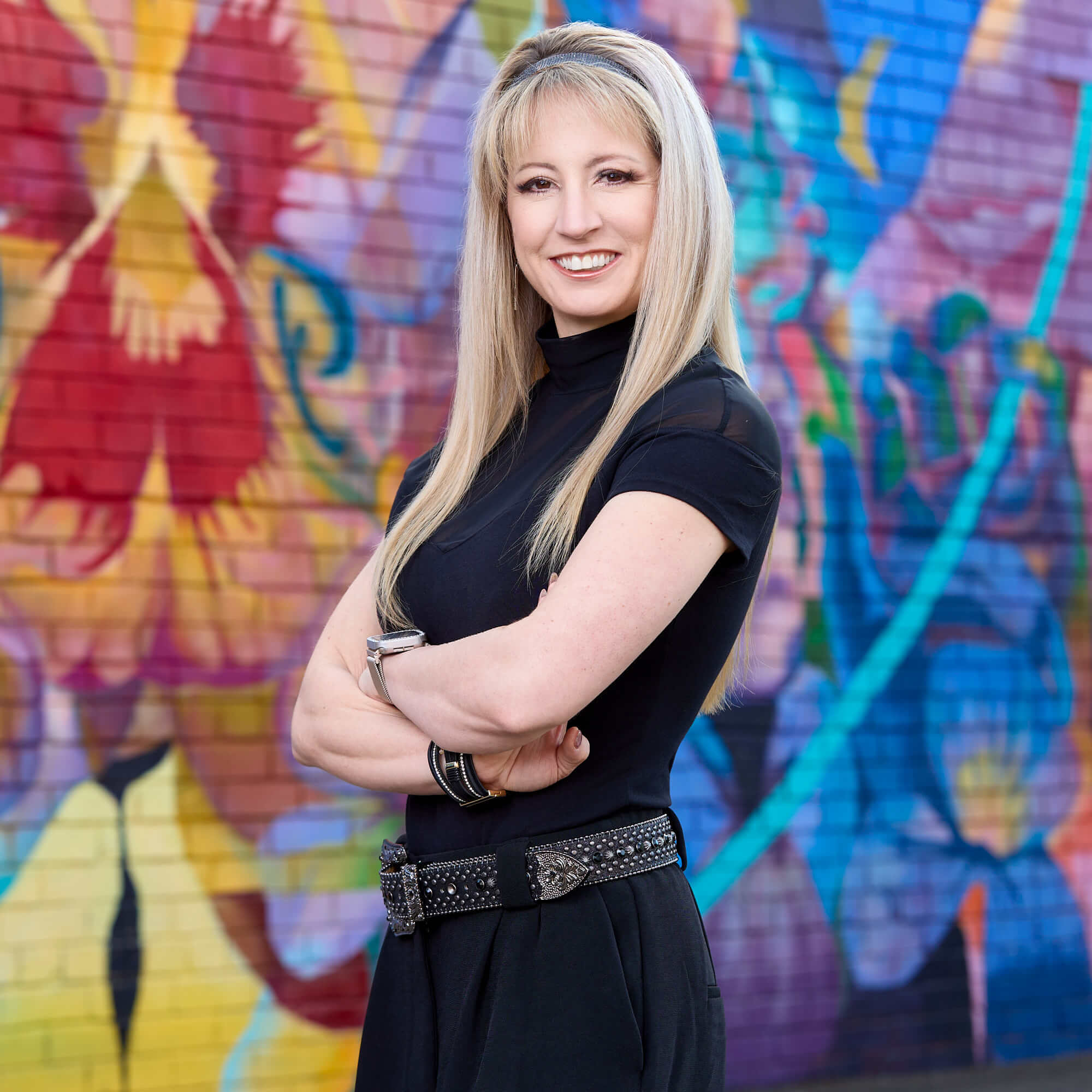 Aleigha Tucker Lead Photographer Portrait – Charlotte Commercial Photography Outdoor environmental portrait of Aleigha Tucker, lead photographer at Fenix Fotography, wearing a black top and posing with arms crossed in front of a colorful mural in Charlotte, NC.